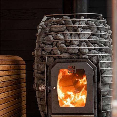 Side view of HUUM HIVE Wood 17kW Wood Sauna Stove installed in traditional sauna with stone walls