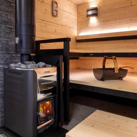 A person adding wood to the Harvia PRO Series 31kW Sauna Wood Sauna Stove Pro 36 to create a cozy and relaxing sauna experience